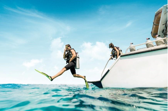 Person jumping from a yacht into turquoise Bahamian waters wearing a wetsuit for snorkeling and diving adventure.